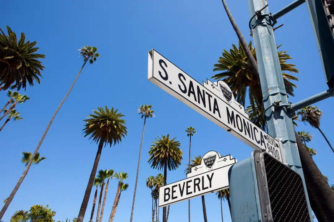 Street sign at the intersection of South Santa Monica Boulevard and Beverly Drive with palm trees and clear sky, in East Los Angeles.