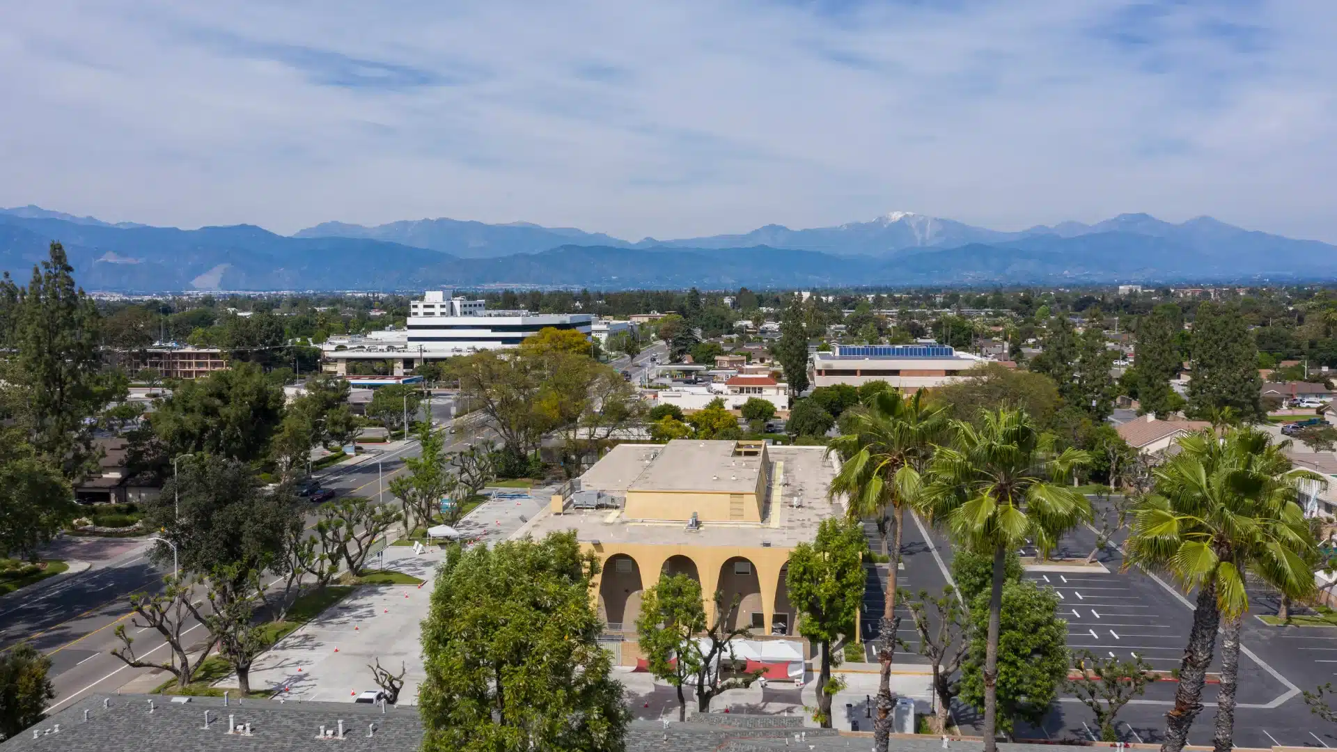 Wide view of West Covina with tree-lined neighborhoods, surrounding foothills, and a bright daytime sky typical of Southern California.